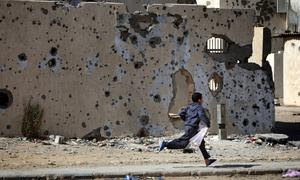 Un niño corre frente a edificios dañados por los bombardeos en la ciudad libia de Sirte.