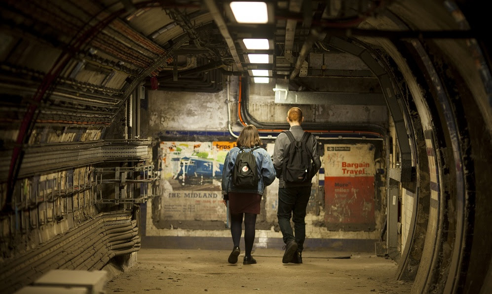 Two people wearing backpacks looking at historic, torn posters on tunnel wall