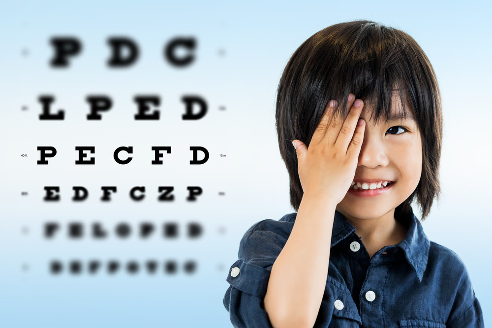 eye chart and a smiling boy covering one eye with his hand