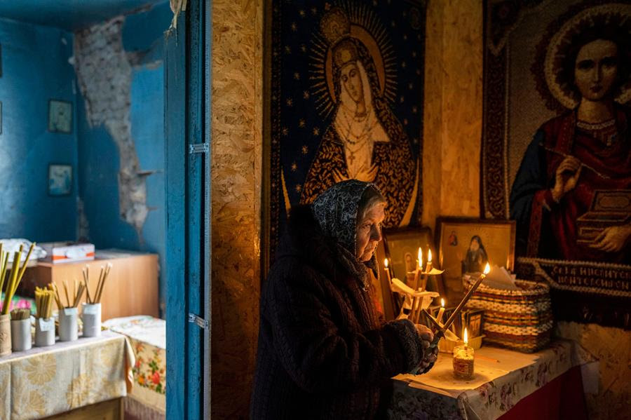 A woman lights candles as part of a Good Friday ceremony inside the damaged Pokrova church, during Orthodox Easter, on the outskirt of Chernihiv, Ukraine. There are images of religious figures on the table beside her and on the walls surrounding her.