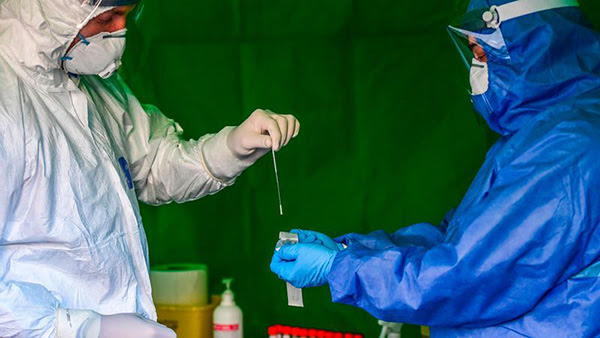 A pair of medical workers in protective gear prepare to perform drive-through swabbing tests for coronavirus