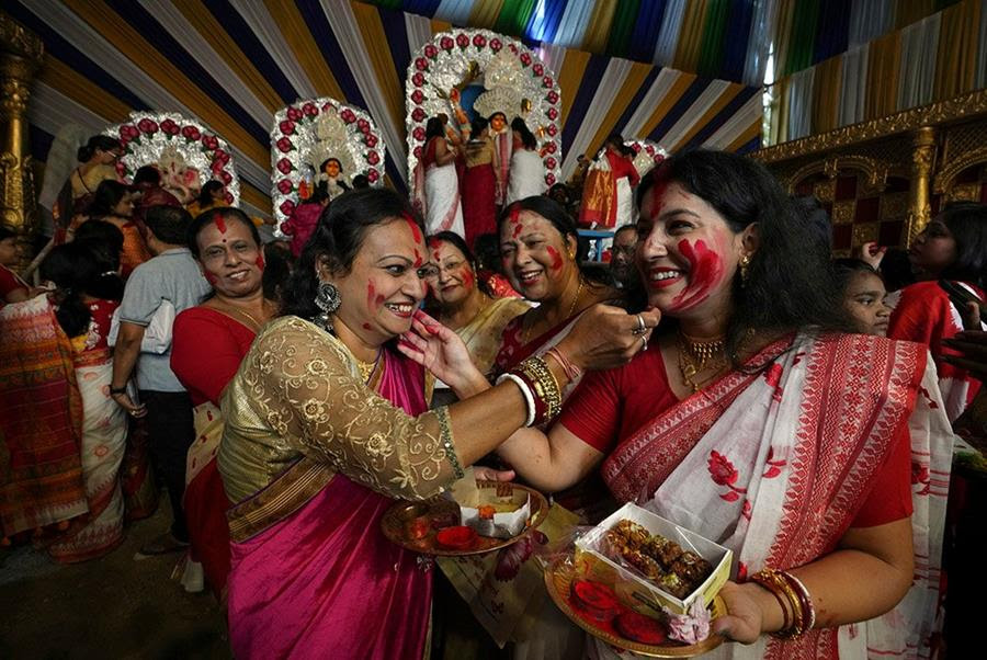 Hindu women put vermilion powder on each other's faces during Durga Puja festival. They are smiling happily.