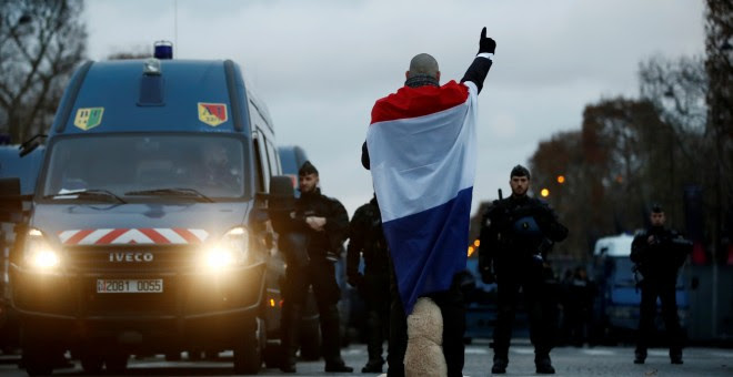 Un hombre arropado con la bandera de Francia mira de frente a la Policía. REUTERS/Christian Hartmann