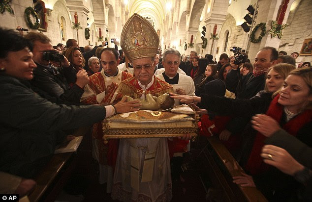 Latin Patriarch of Jerusalem Fouad Twal carries the statuette of baby Jesus during the midnight Mass ceremony which marks the beginning of Christmas Day at the Church of the Nativity in Bethlehem