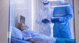 healthcare providers in full PPE talking to patient in hospital bed