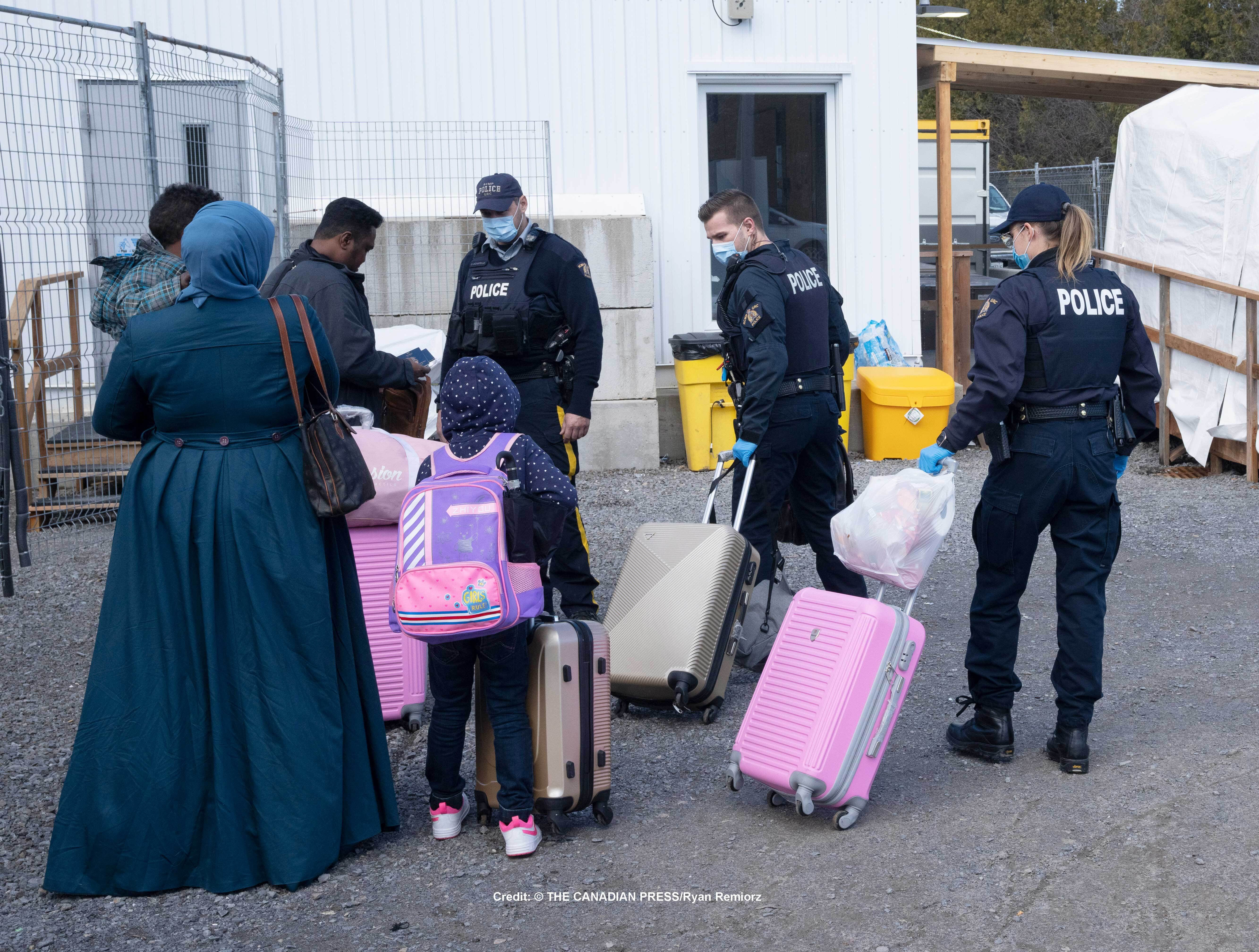 RCMP officers help asylum seekers as they cross the border into Canada at Roxham Road on March 24, 2023.
