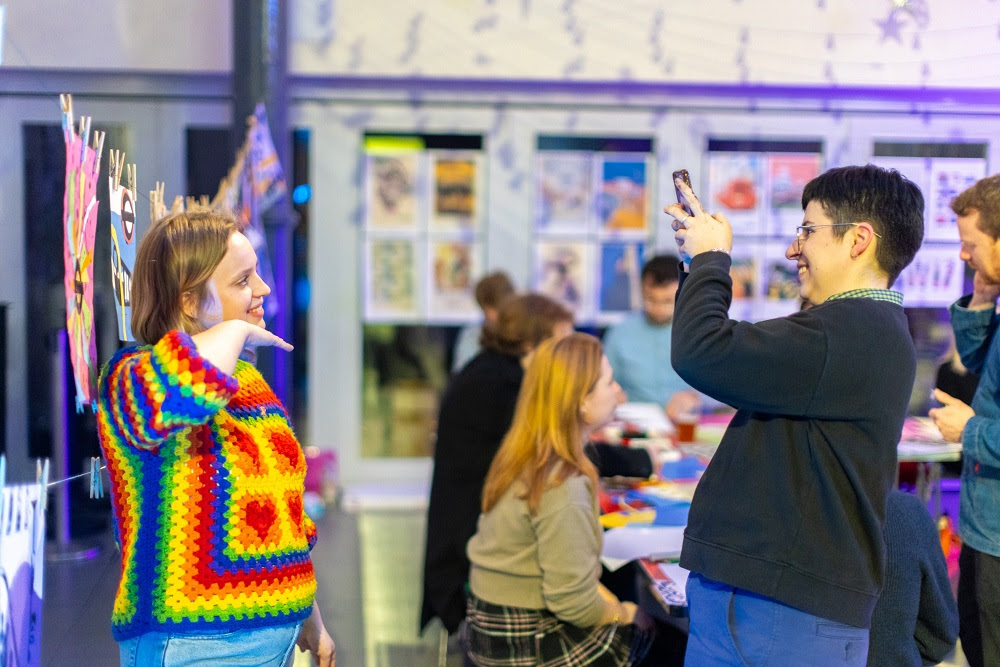 Visitor taking a photo of another visitor wearing rainbow jumper in a gallery
