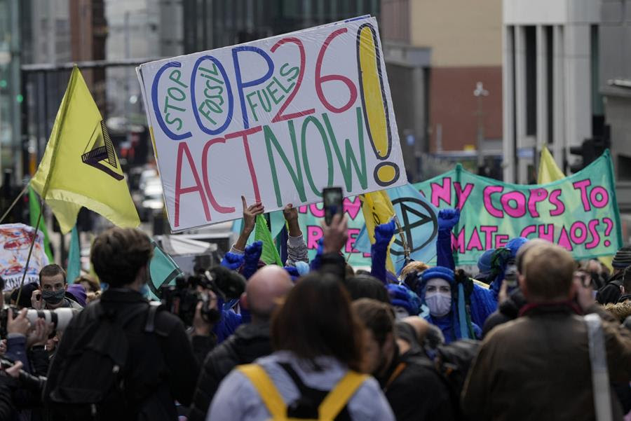 Someone holds a sign that says "COP26 Act Now!" above a crowd of people. Between the other words on the sign are the words, "Stop fossil fuels."