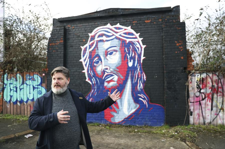 Jonny Clark, program manager for public theology at Corrmeela, an organisation that has worked for decades toward reconciliation in Northern Ireland, visits the peace walls in west Belfast, Northern Ireland. There is a mural of Jesus behind him.