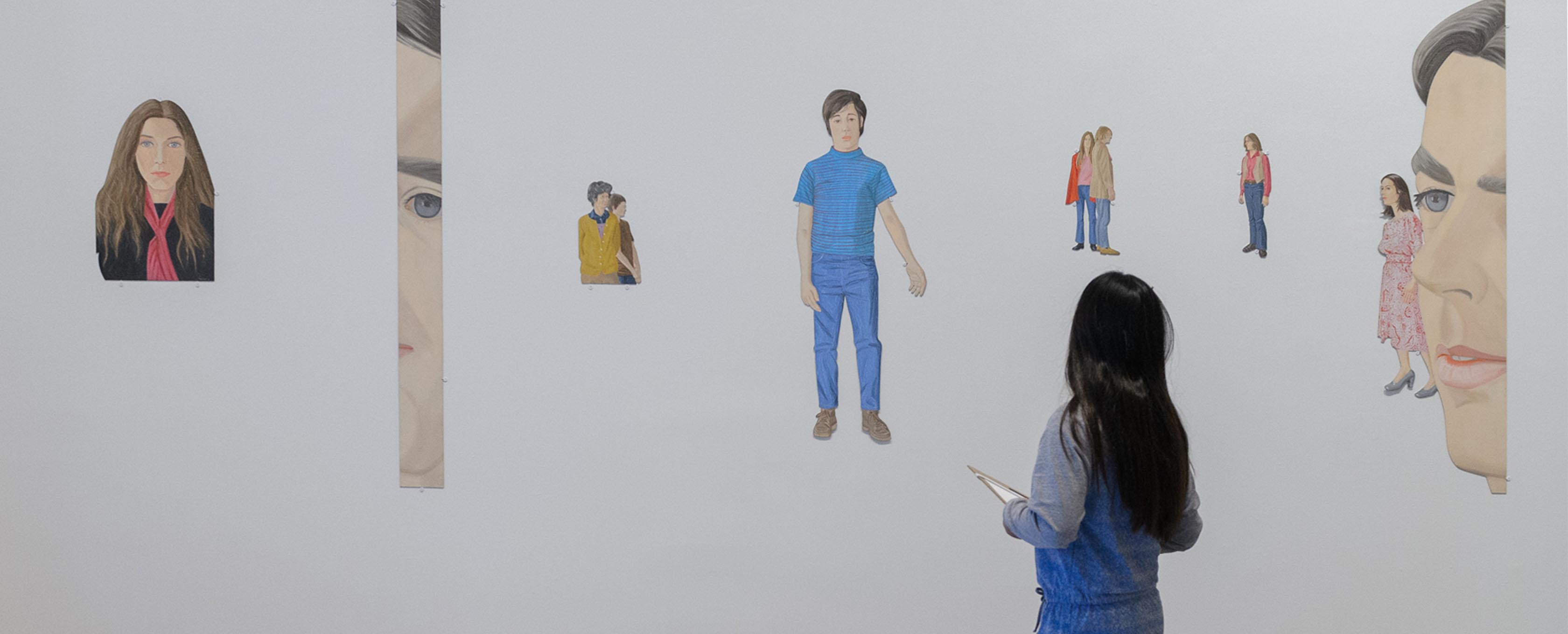 Uma garota fica na frente de desenhos de pessoas.