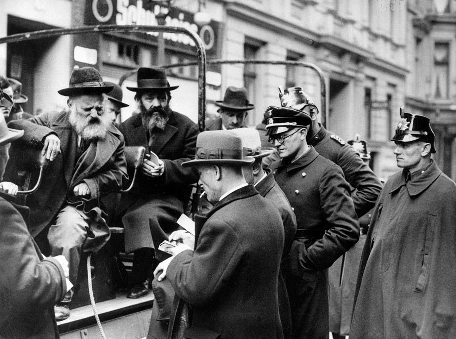 A black and white photo of a busload of arrested Jewish men being questioned by government officials in Germany.