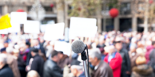 A microphone in the foreground, with a crowd of people in the background.