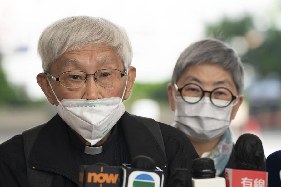 Cardinal Joseph Zen speaks to members of the media. He is wearing a mask. There are several microphones in front of him.