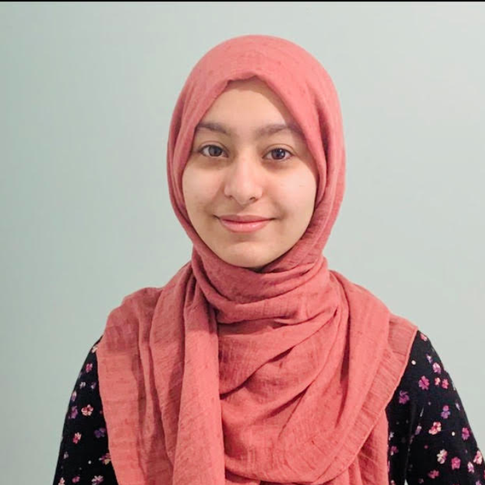 Headshot of Zainab Khan who is smiling and wearing a black floral top and pink hijab.