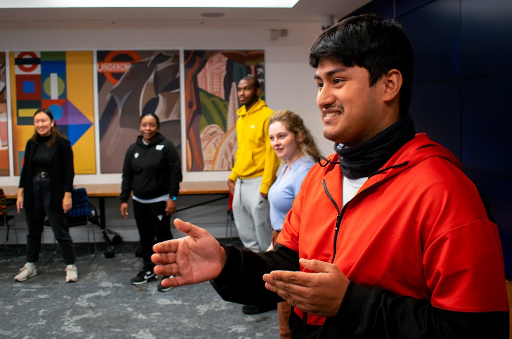 Young person in orange top talking with a group of young people in a circle