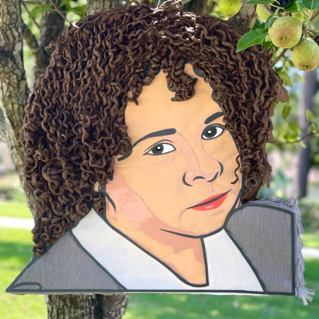 A flat piñata created to resemble a 1995 photograph of Yolanda Saldívar. Her hair is made of tightly coiled brown tissue paper, to resemble Ms. Saldívar’s curls, and she wears a gray blazer.
