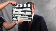 Screen grab of a clapperboard in front of Office of Workers’ Compensation Program Director Chris Godfrey, sitting in front of a plain backdrop. 