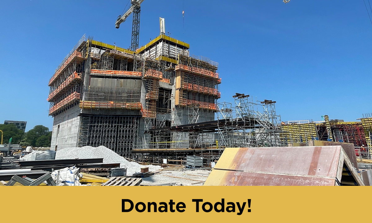 A construction site with partially built buildings, cranes, and building materials is set against a blue sky. At the bottom, a banner has the words "Donate Today!"