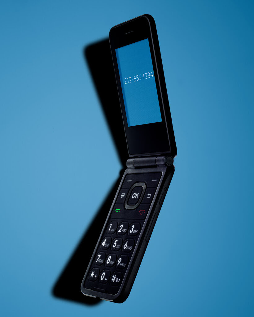 A black flip phone, on its side, open, on a blue background.